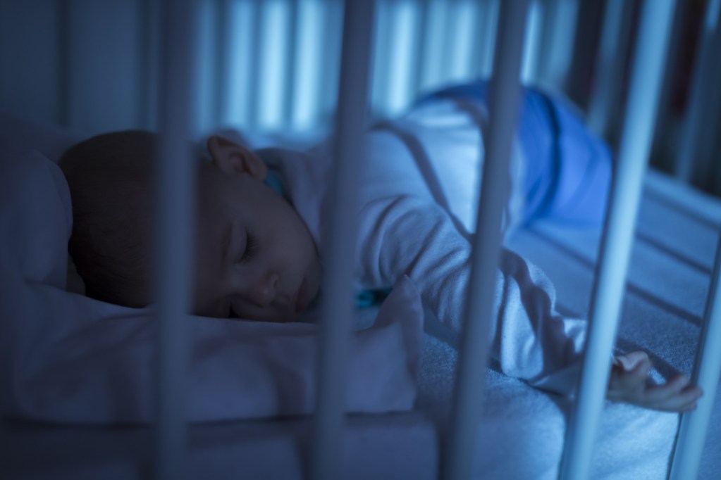 Baby sleeps in crib with blue night light