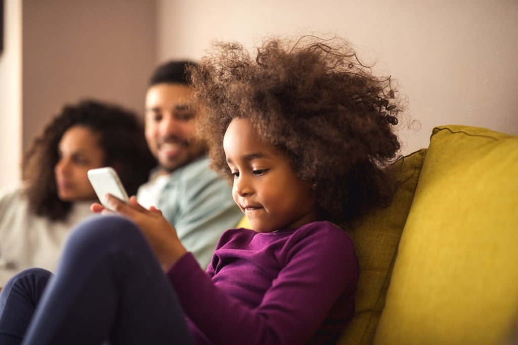 A child on a cellphone while their parents sit next to them.