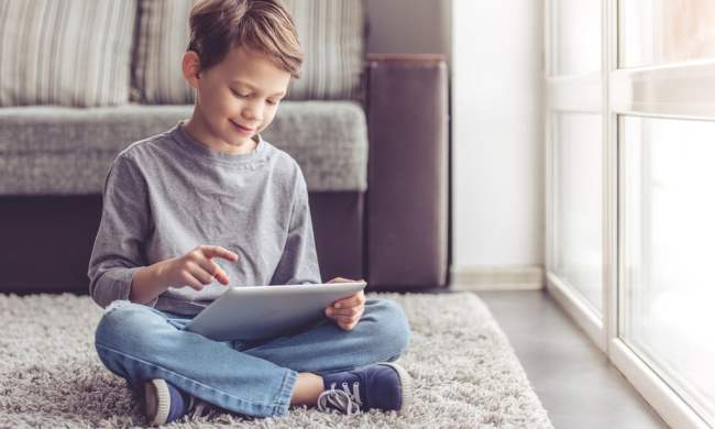 Boy sitting on a floor using a tablet.