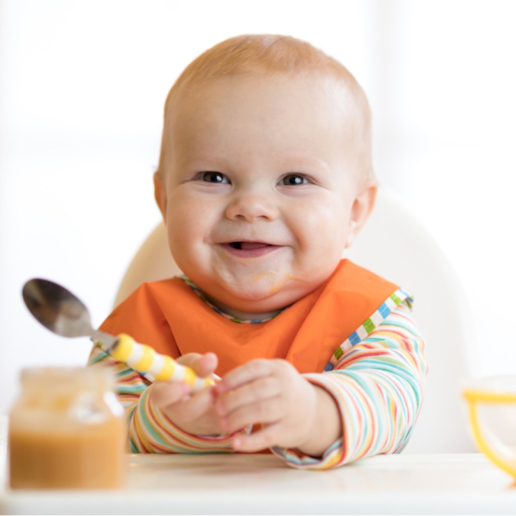 Smiling baby sits in high chair with a spoon
