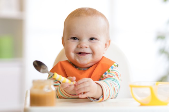Smiling baby sits in high chair with a spoon