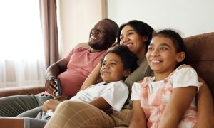 Family of four sitting on a couch watching TV