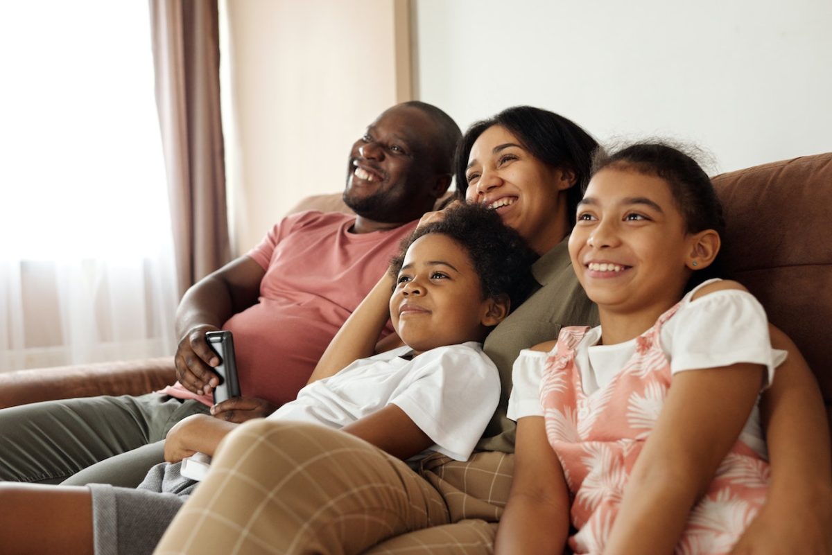 Family of four sitting on a couch watching TV