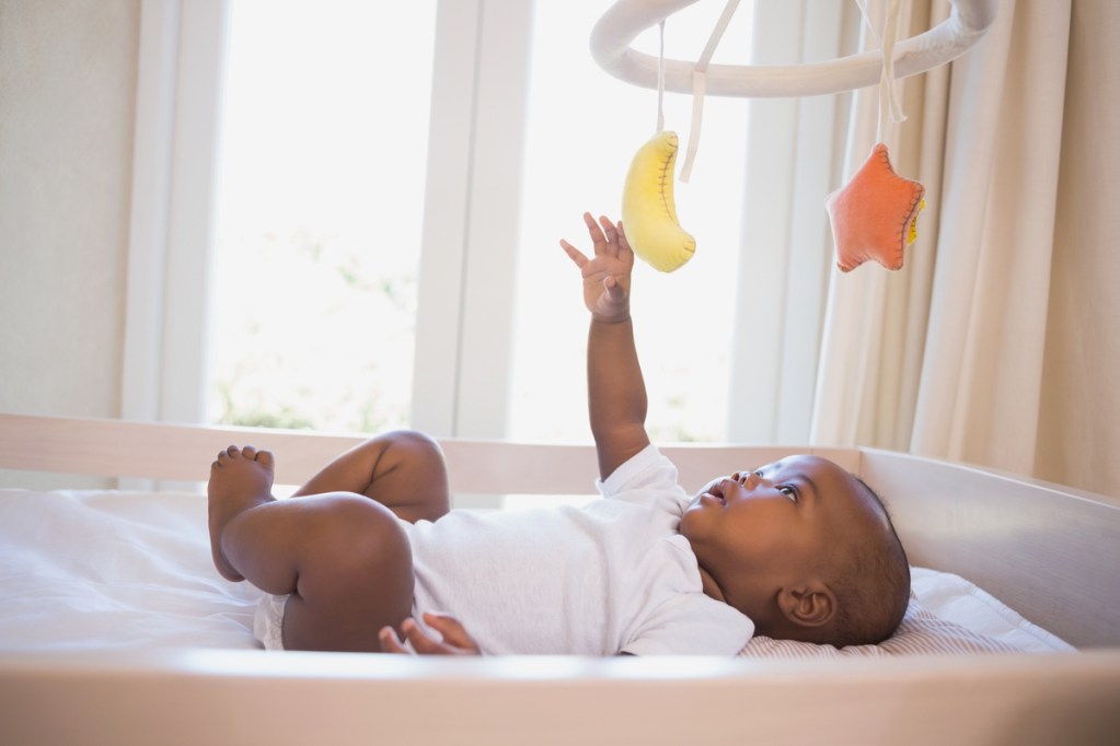 A baby playing with the mobile above their crib.