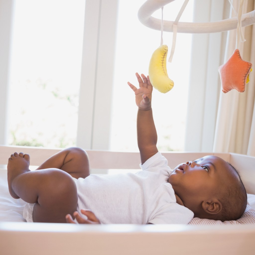 A baby playing with the mobile above their crib