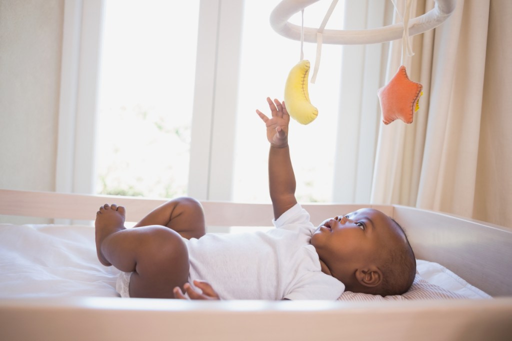 A baby playing with the mobile above their crib.