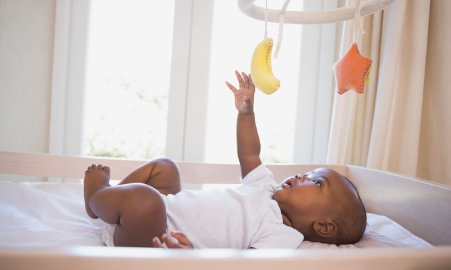 A baby playing with the mobile above their crib