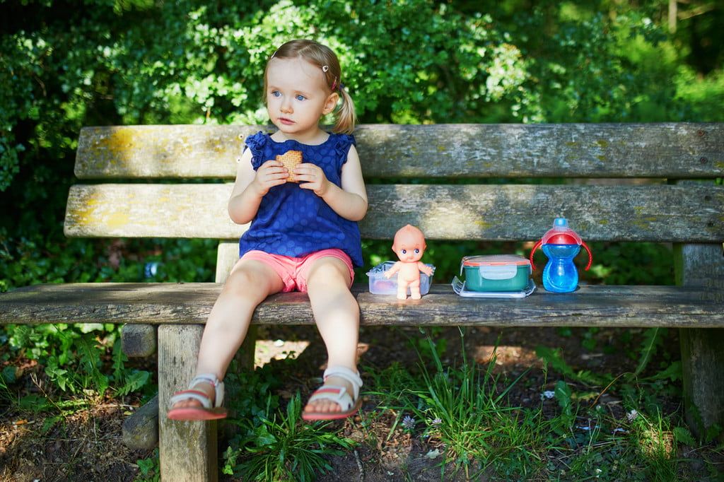 Little girl eating a snack on a bench