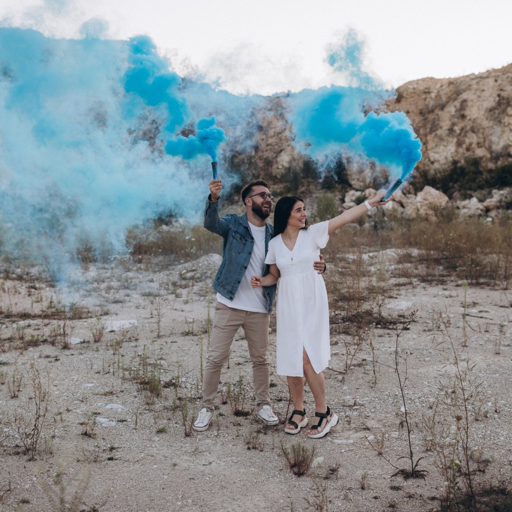 Pregnant couple holding blue smoke cannons celebrating