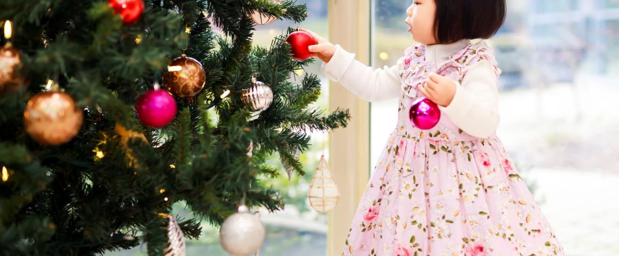 a little girl putting decorations on a Christmas tree