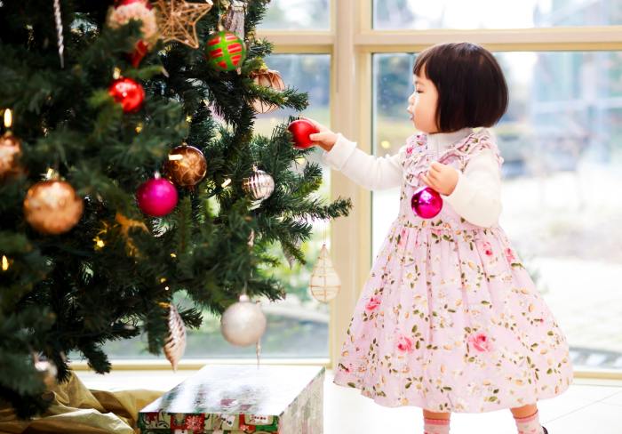 a little girl putting decorations on a Christmas tree