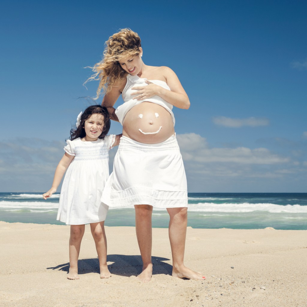 A mother and daughter wear sunscreen at the beach.