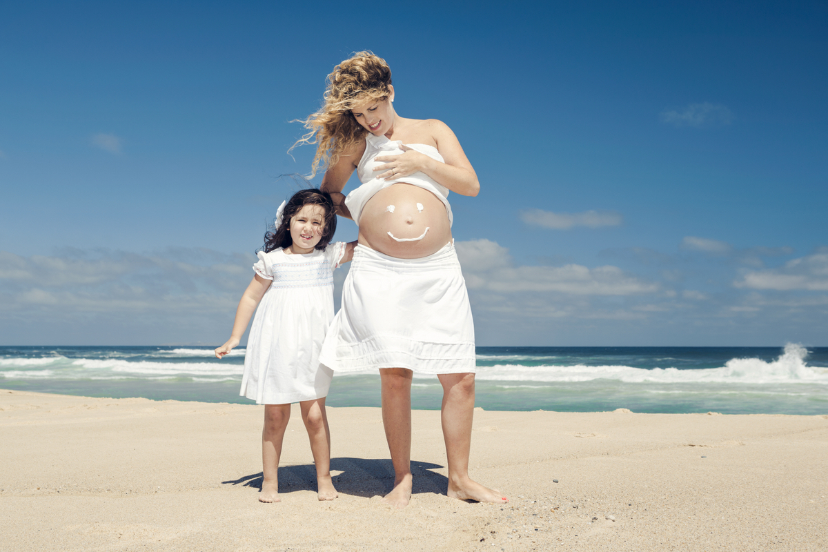 A mother and daughter wear sunscreen at the beach.