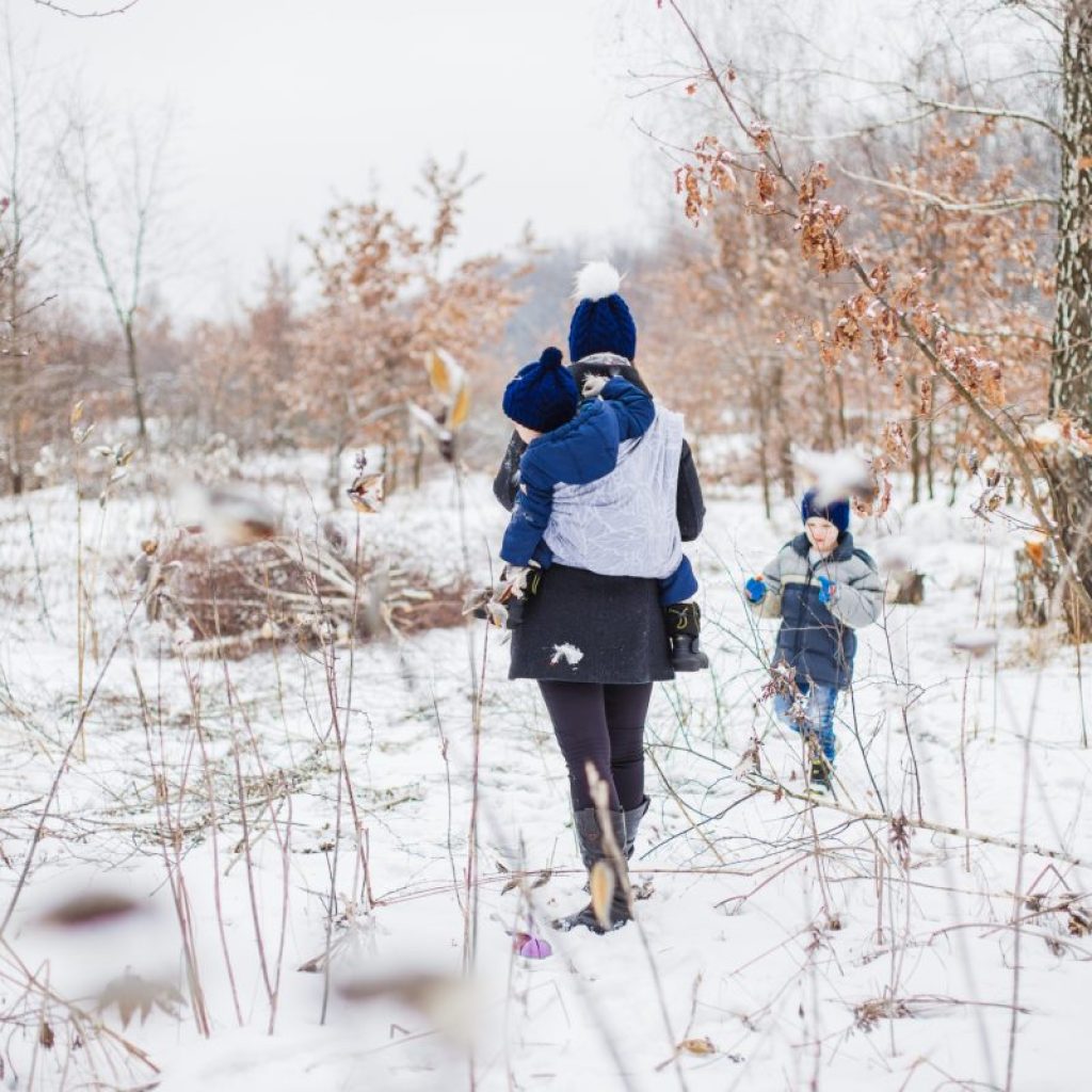 A parent walking with their two children in the snow all bundled up