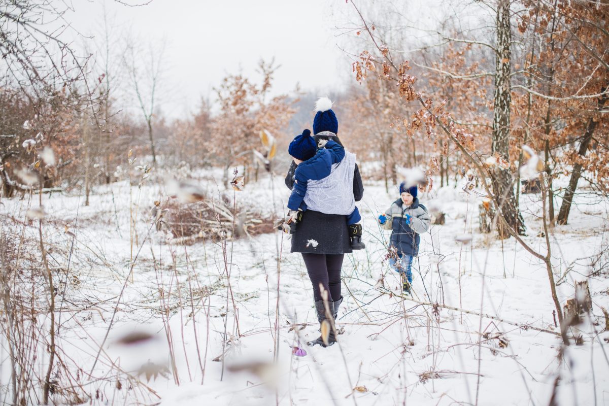A parent walking with their two children in the snow all bundled up