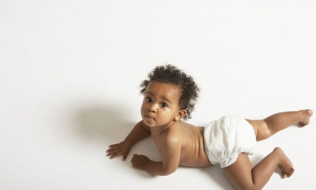 A baby on the floor on their stomach looking over their shoulder.