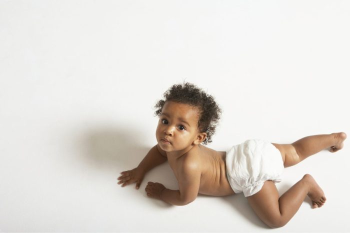 A baby on the floor on their stomach looking over their shoulder.