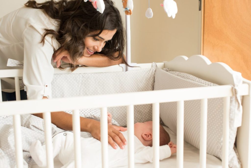 A mother watching her baby sleep in their crib.