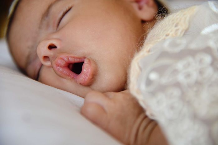 Baby sleeping in a bed with their mouth open