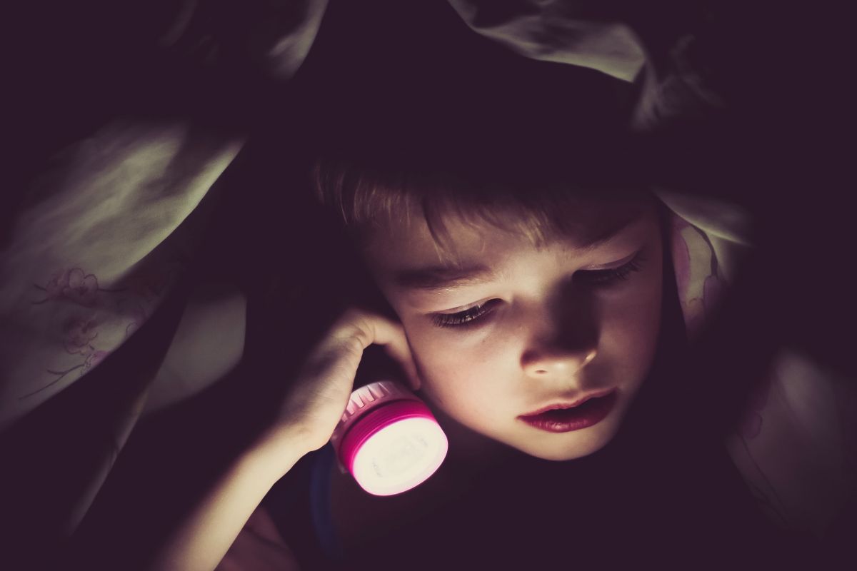 A boy with a flashlight in bed