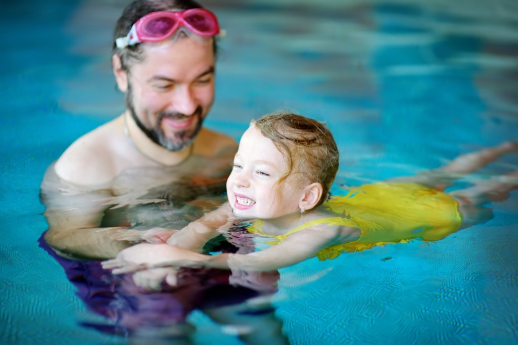Adult teaching child to swim in a pool.