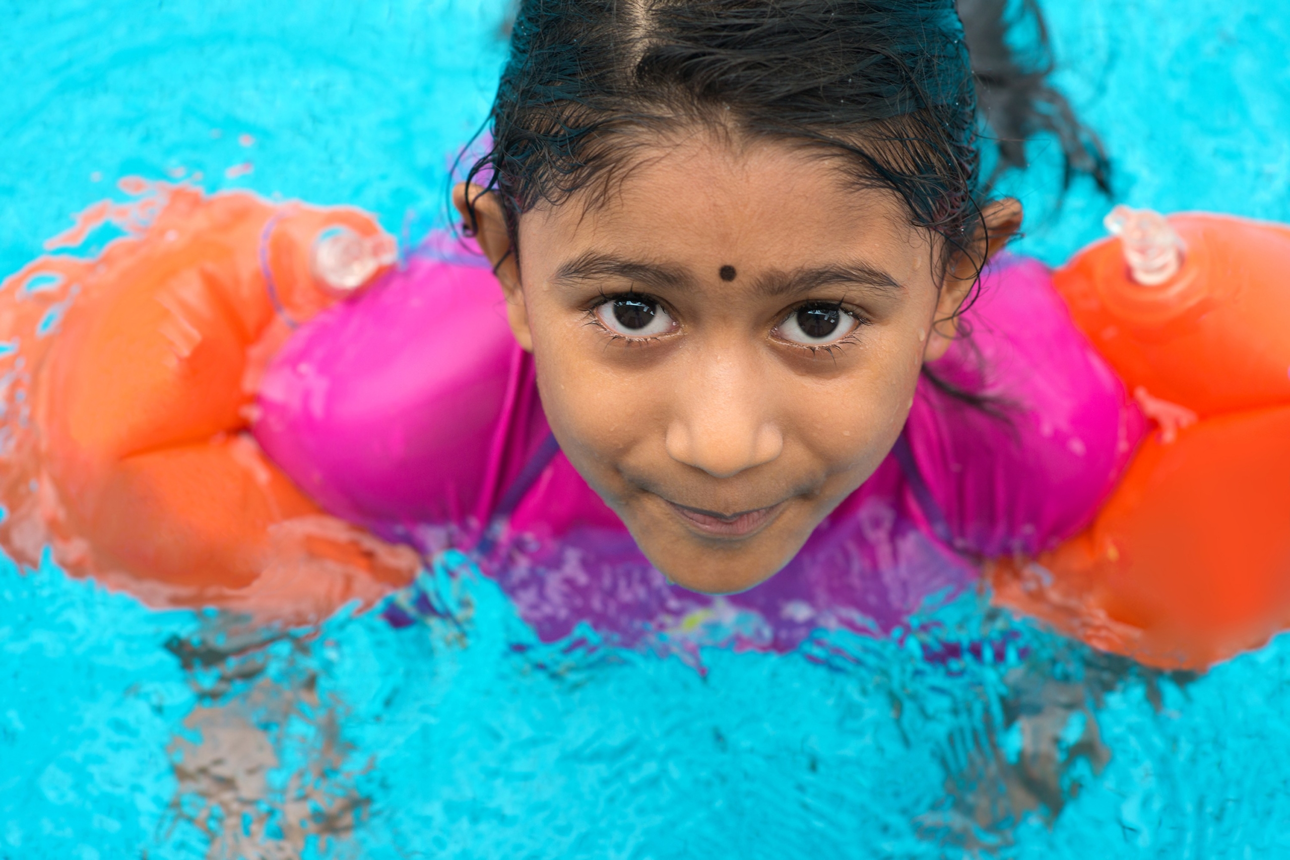 Young Indian girl swimming in a pool with floaties