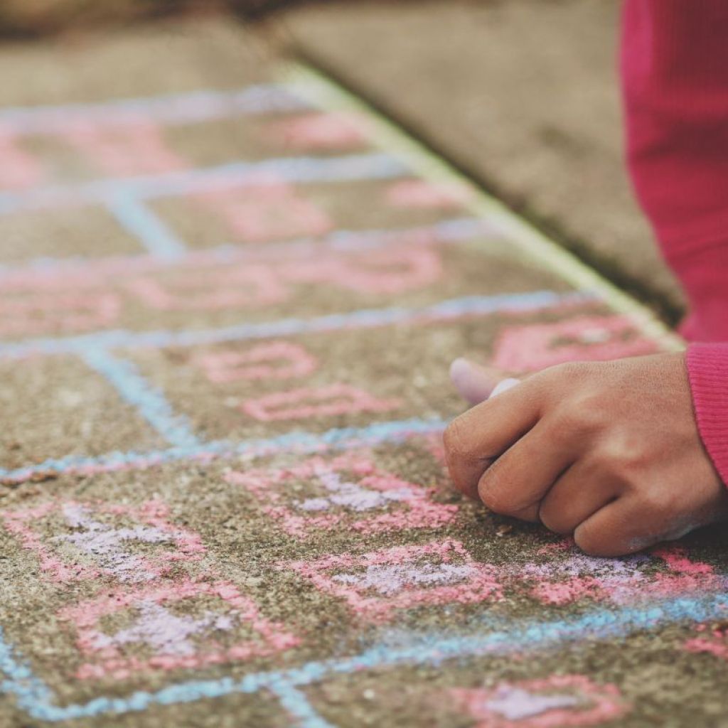 A girl drawing hopscotch with chalk on a sidewalk