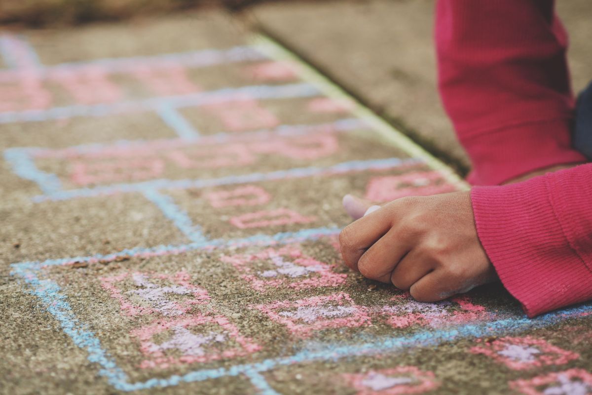 A girl drawing hopscotch with chalk on a sidewalk