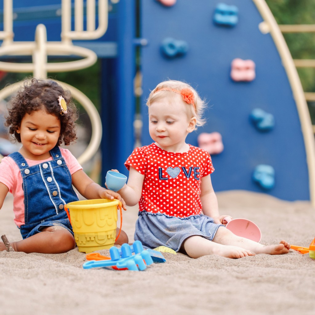 Two toddler girls sharing toys during a park playgroup