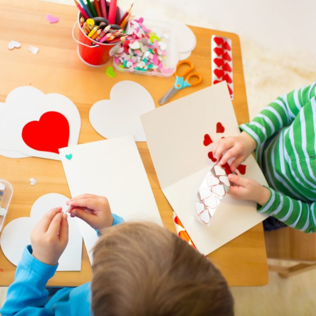 two boys make Valentine's cards at a table full of paper, hearts, and art supplies