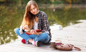A teenager reading a book on a dock