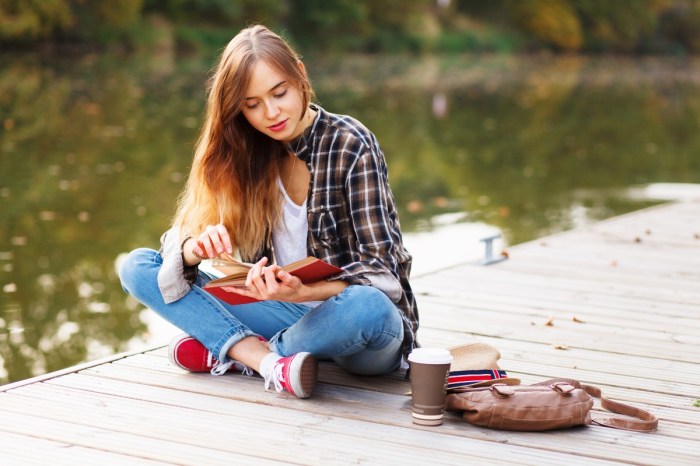 A teenager reading a book on a dock