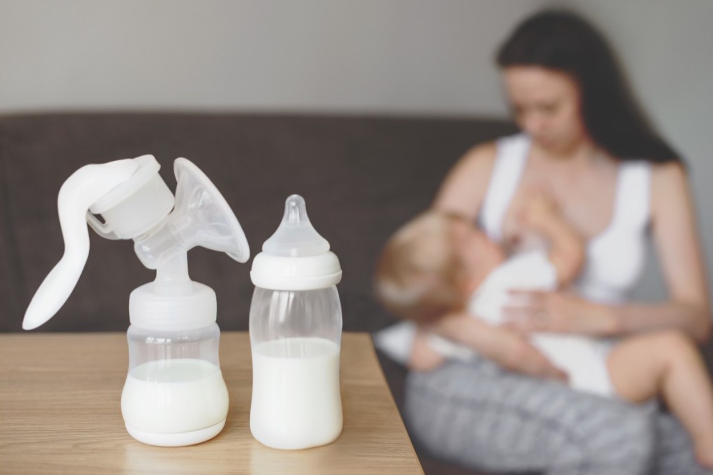 Mom breastfeeding and manual breast pump on the table