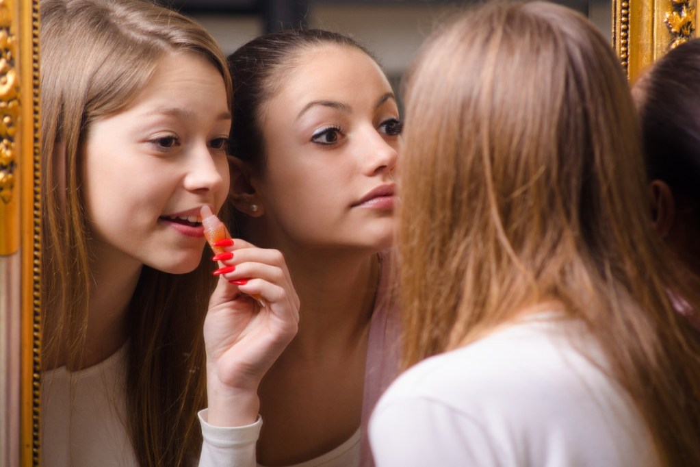 Two teens applying makeup in a mirror