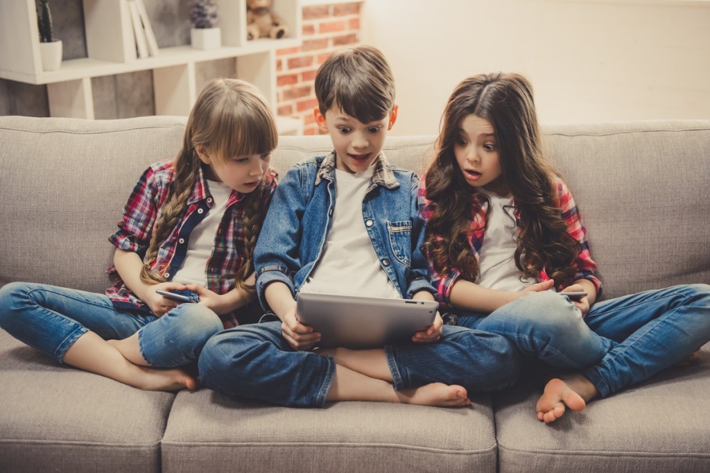 Kids on a couch playing on smart devices.