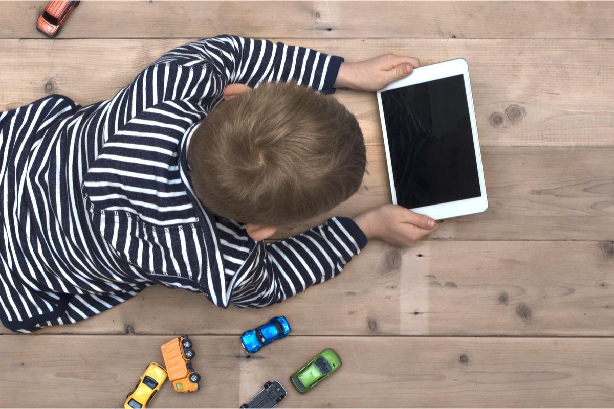 A boy with a tablet and toy cars