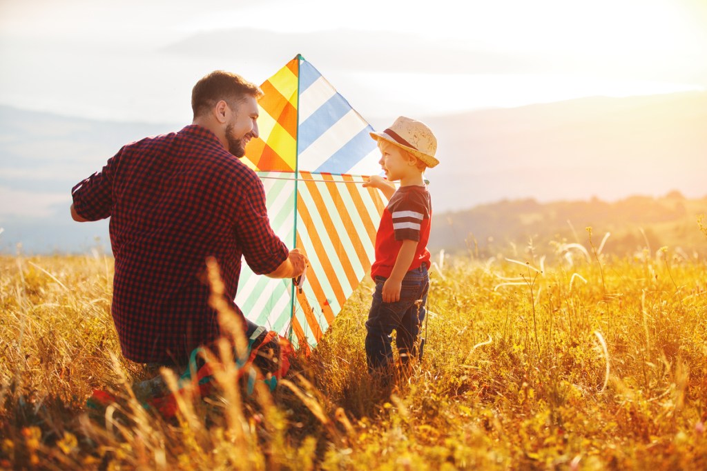 father and son having fun flying a kite in a field