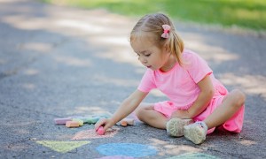 Girl drawing outside with sidewalk chalk