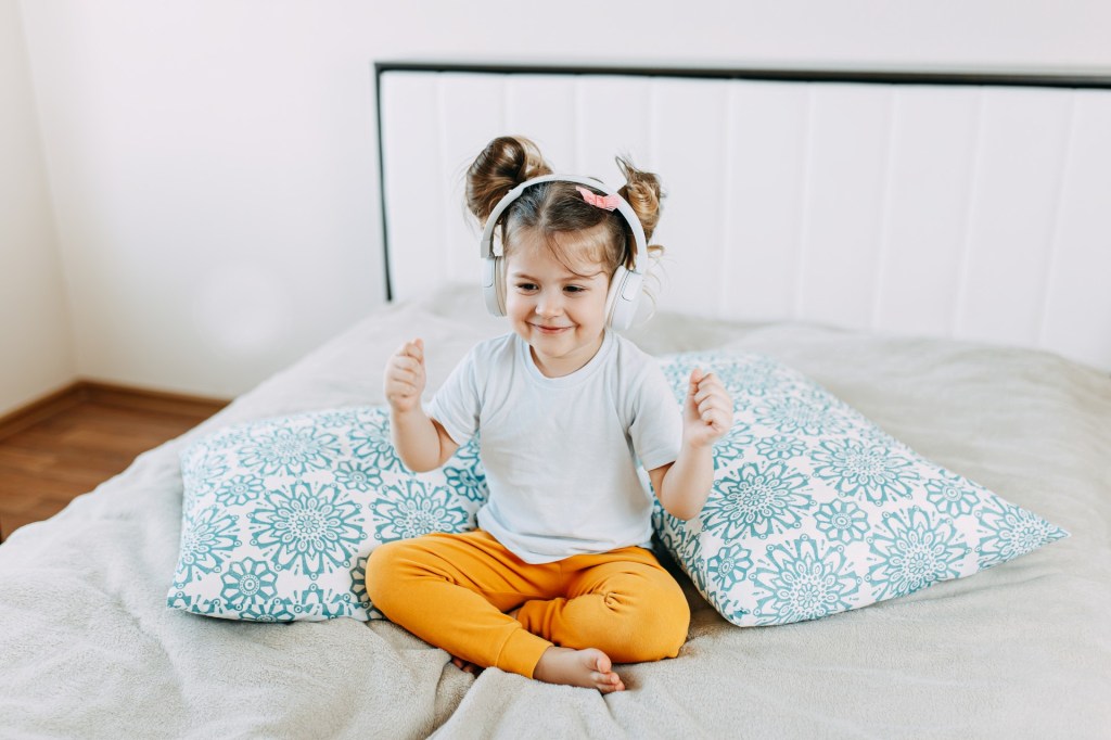 Little girl wearing headphones on a bed
