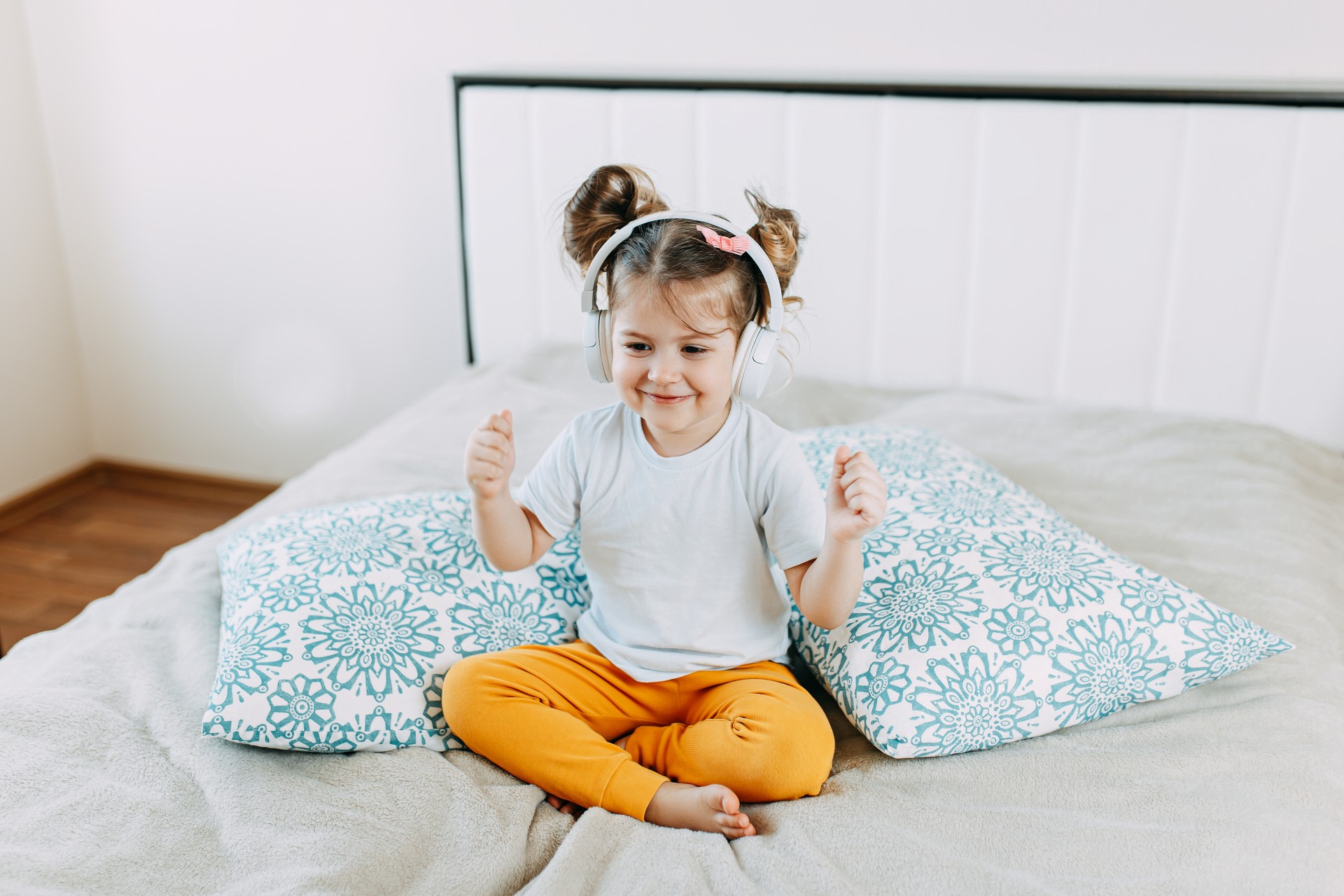 Little girl wearing headphones on a bed
