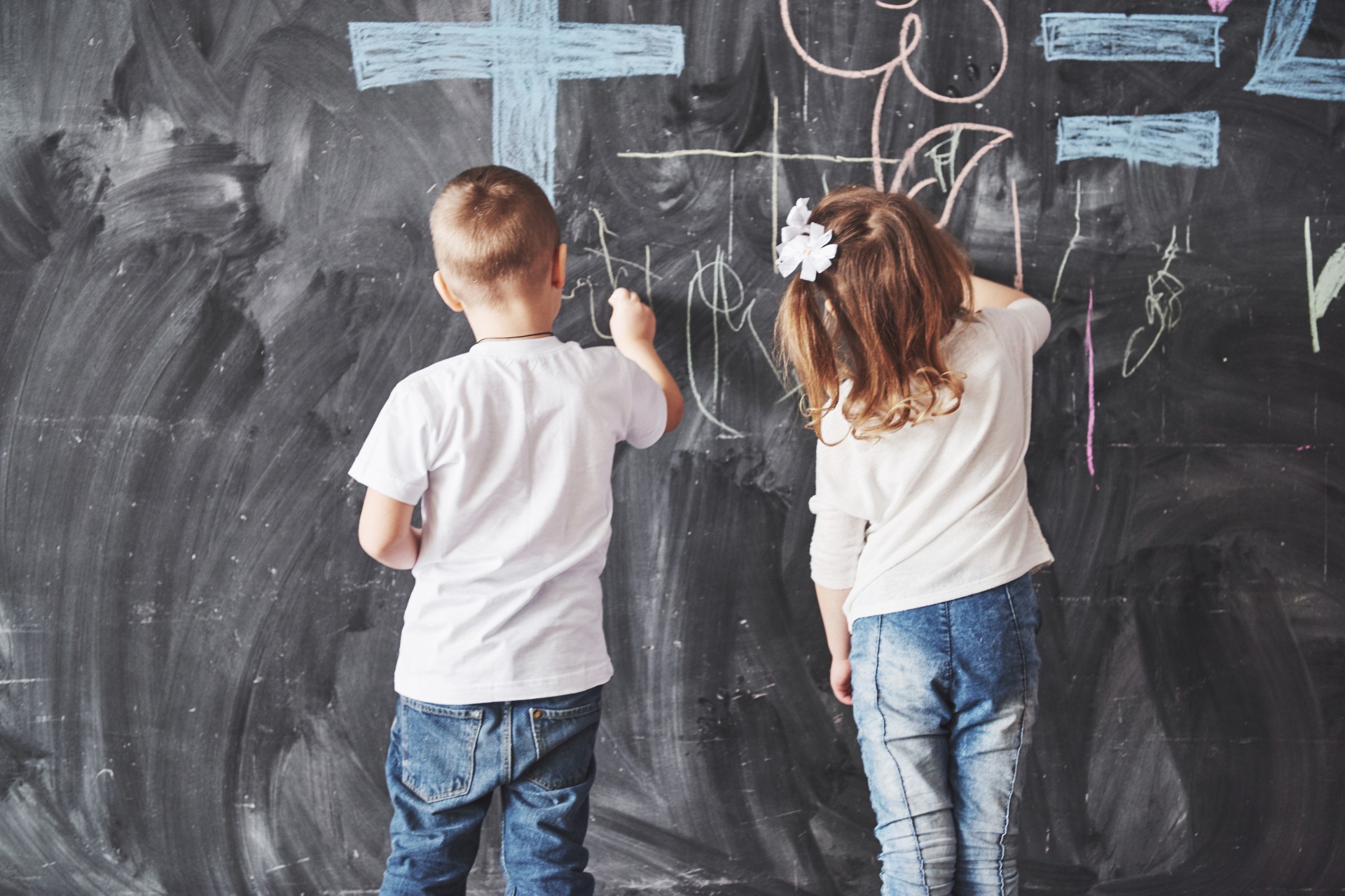 Two kids coloring on a chalkboard wall