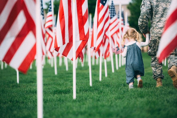 A little girl with a service member near American flags in the ground