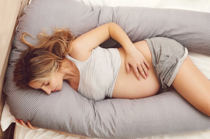 A pregnant woman sleeping with a pregnancy pillow.