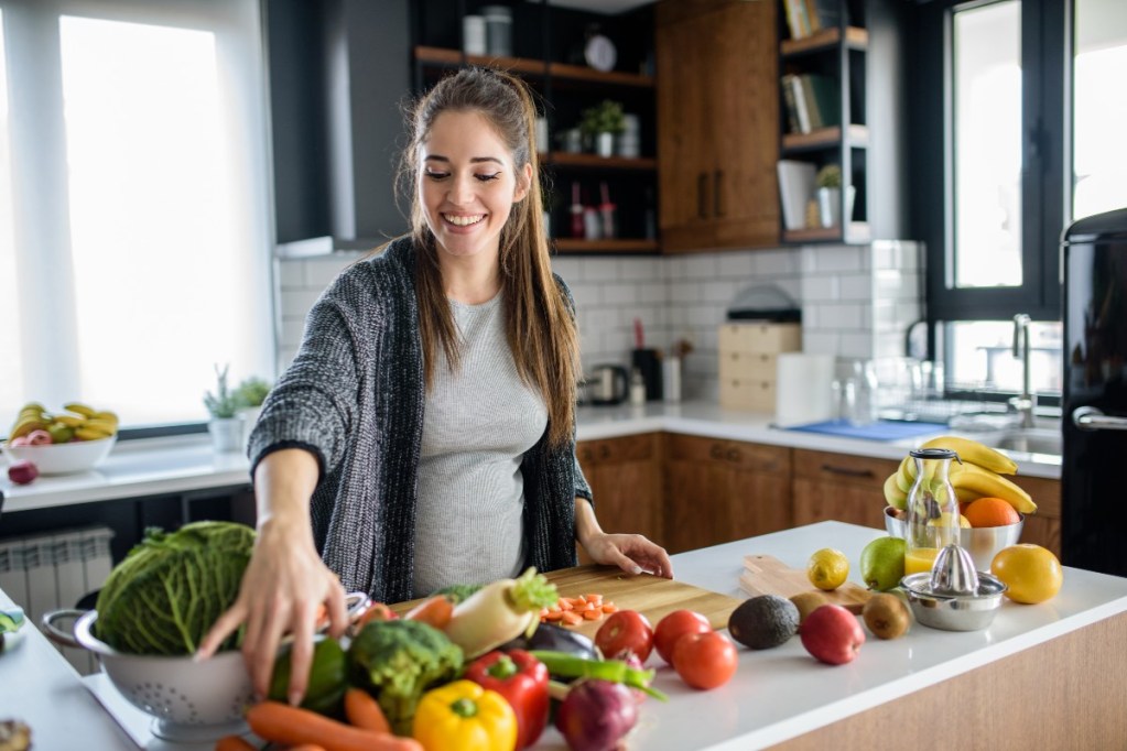 Pregnant woman cooking with fruits and vegetables.