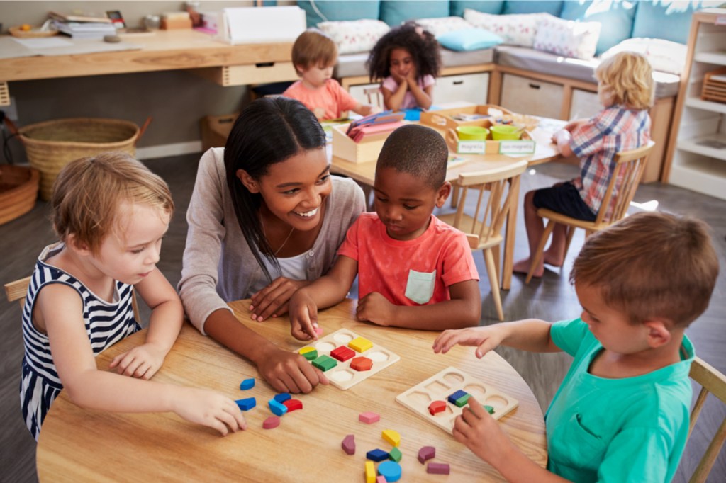 Preschool teacher talking with students at a table.