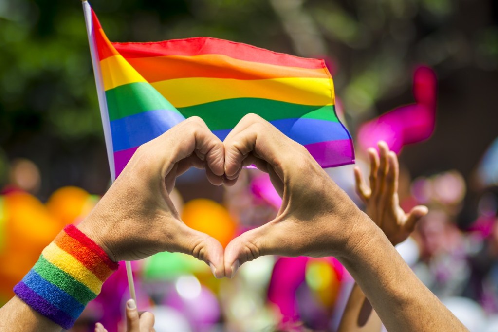 Person at Pride parade making a heart with their hands.