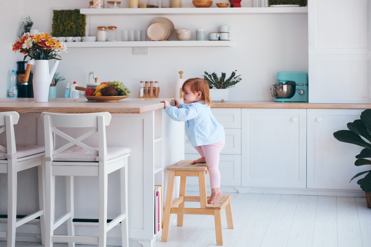 A toddler using a step stool in a kitchen