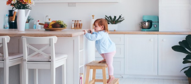 A toddler using a step stool in a kitchen