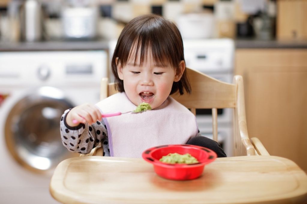 Baby in highchair eating avocado puree