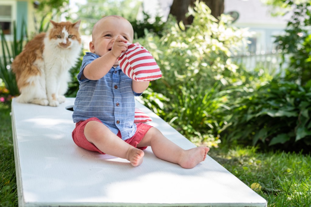 Baby and a cat sitting on a cornhole game